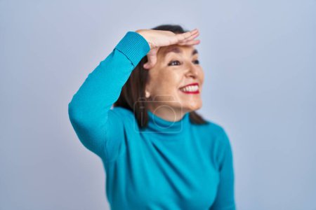 Photo for Middle age hispanic woman standing over isolated background very happy and smiling looking far away with hand over head. searching concept. - Royalty Free Image