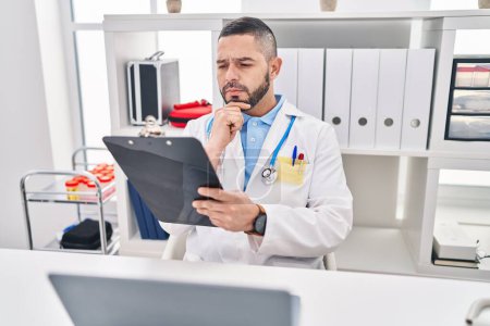 Photo for Young latin man doctor using laptop reading medical report at clinic - Royalty Free Image