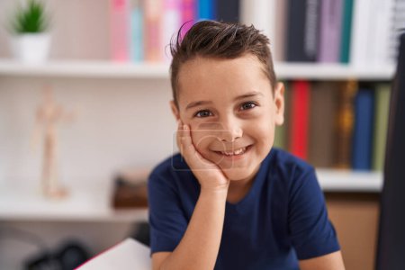 Téléchargez les photos : Adorable bambin hispanique souriant confiant assis sur la table à l'école de la bibliothèque - en image libre de droit