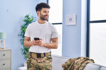 Photo for Young arab man army soldier using smartphone standing at home - Royalty Free Image