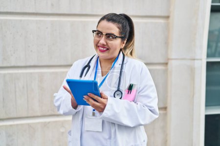 Foto de Young beautiful plus size woman doctor smiling confident using touchpad at hospital - Imagen libre de derechos