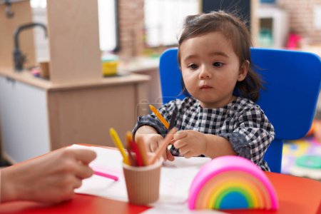 Photo for Adorable chinese girl preschool student sitting on table drawing on paper at kindergarten - Royalty Free Image