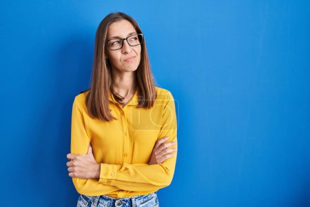 Téléchargez les photos : Jeune femme portant des lunettes debout sur fond bleu souriant regardant vers le côté et regardant loin en pensant. - en image libre de droit