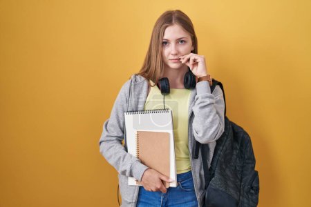 Téléchargez les photos : Young caucasian woman wearing student backpack and holding books mouth and lips shut as zip with fingers. secret and silent, taboo talking - en image libre de droit