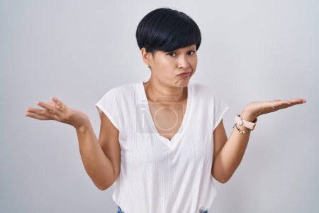 Photo for Young asian woman with short hair standing over isolated background clueless and confused expression with arms and hands raised. doubt concept. - Royalty Free Image