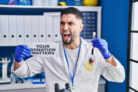 Photo for Young handsome man working at scientist laboratory holding blood sample angry and mad screaming frustrated and furious, shouting with anger. rage and aggressive concept. - Royalty Free Image