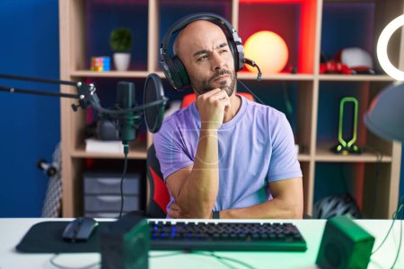 Téléchargez les photos : Middle age bald man playing video games wearing headphones thinking concentrated about doubt with finger on chin and looking up wondering - en image libre de droit