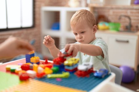 Photo for Adorable toddler playing with car and toy and construction blocks sitting on table at kindergarten - Royalty Free Image