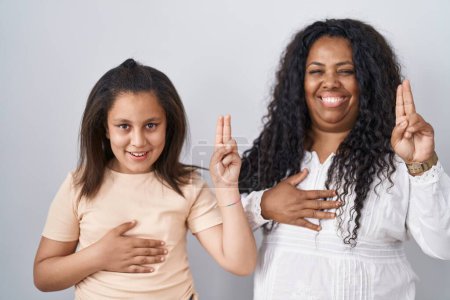 Photo for Mother and young daughter standing over white background smiling swearing with hand on chest and fingers up, making a loyalty promise oath - Royalty Free Image