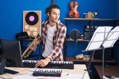Photo for Young hispanic man musician composing song holding trumpet at music studio - Royalty Free Image