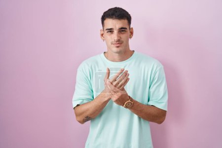 Foto de Hombre hispano guapo de pie sobre fondo rosa sufriendo dolor en las manos y los dedos, inflamación de la artritis - Imagen libre de derechos
