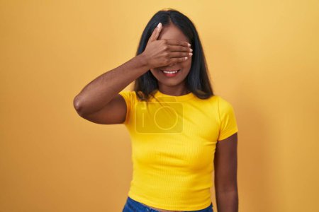 Photo for Young indian woman standing over yellow background smiling and laughing with hand on face covering eyes for surprise. blind concept. - Royalty Free Image