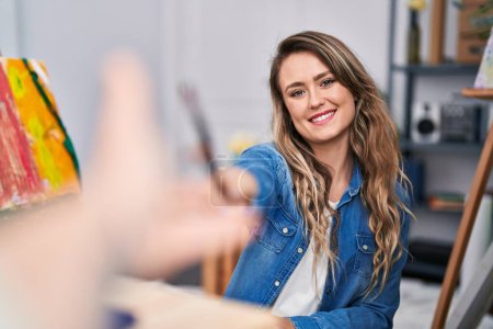 Téléchargez les photos : Jeune femme artiste souriant confiant tenant pinceau au studio d'art - en image libre de droit