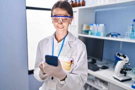 Téléchargez les photos : Young caucasian woman scientist smiling confident using smartphone at laboratory - en image libre de droit