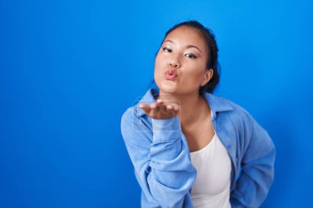 Photo for Asian young woman standing over blue background looking at the camera blowing a kiss with hand on air being lovely and sexy. love expression. - Royalty Free Image