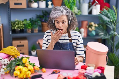 Téléchargez les photos : Middle age woman with grey hair working at florist with laptop covering mouth with hand, shocked and afraid for mistake. surprised expression - en image libre de droit