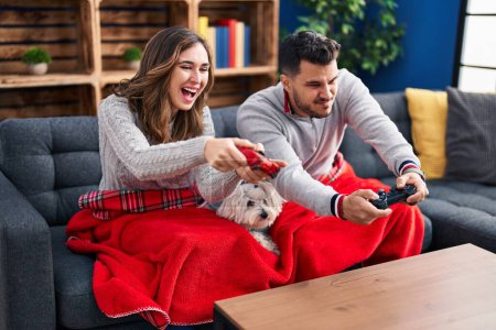 Photo for Man and woman playing video game sitting on sofa with dog at home - Royalty Free Image