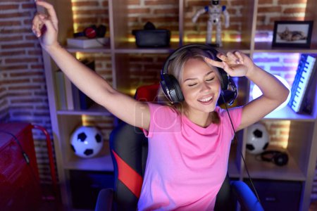 Téléchargez les photos : Jeune femme blonde streamer jouer jeu vidéo avec l'expression gagnante à la salle de jeux - en image libre de droit