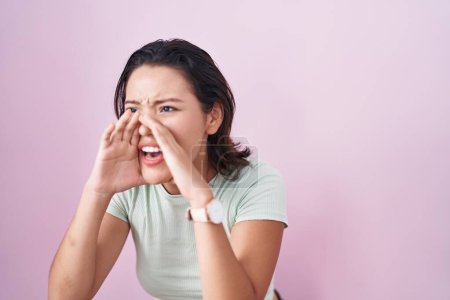 Téléchargez les photos : Hispanic young woman standing over pink background shouting angry out loud with hands over mouth - en image libre de droit