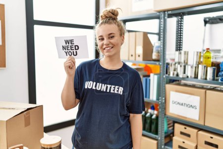 Photo for Young caucasian woman volunteer holding we need you banner looking positive and happy standing and smiling with a confident smile showing teeth - Royalty Free Image