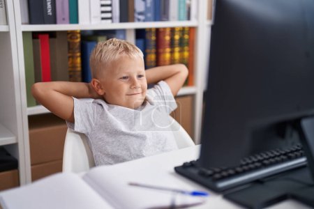 Téléchargez les photos : Adorable enfant en bas âge utilisant un ordinateur détendu sur la table en classe - en image libre de droit