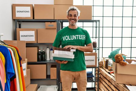 Photo for Middle age grey-haired man volunteer smiling confident holding books at charity center - Royalty Free Image