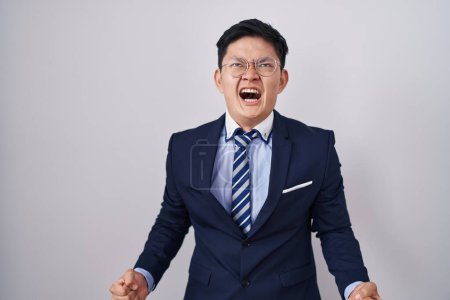 Téléchargez les photos : Young asian man wearing business suit and tie angry and mad screaming frustrated and furious, shouting with anger. rage and aggressive concept. - en image libre de droit