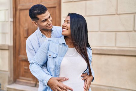 Téléchargez les photos : Jeune couple latin s'attendant bébé se câlinant debout à la rue - en image libre de droit