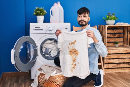 Photo for Young hispanic man with beard holding clean white t shirt and t shirt with dirty stain smiling looking to the side and staring away thinking. - Royalty Free Image