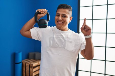 Photo for Hispanic young man using dumbbells surprised with an idea or question pointing finger with happy face, number one - Royalty Free Image