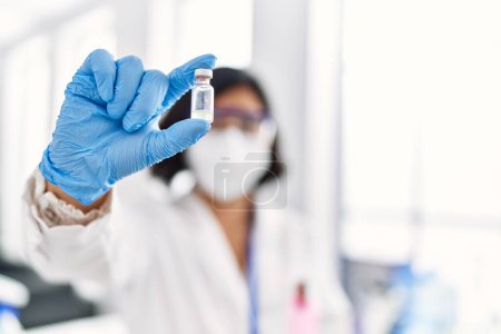 Photo for Young latin woman wearing scientist uniform and medical mask holding dose vaccine at laboratory - Royalty Free Image