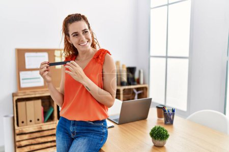 Téléchargez les photos : Jeune rousse femme souriant confiant en utilisant des ongles à la chaux au bureau - en image libre de droit