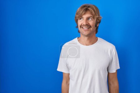 Téléchargez les photos : Middle age man standing over blue background smiling looking to the side and staring away thinking. - en image libre de droit