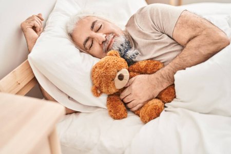 Photo for Middle age grey-haired man hugging teddy bear lying on bed sleeping at bedroom - Royalty Free Image