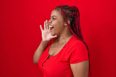 Téléchargez les photos : African american woman with braided hair standing over red background shouting and screaming loud to side with hand on mouth. communication concept. - en image libre de droit