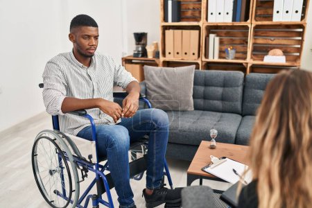 Téléchargez les photos : African american man doing therapy sitting on wheelchair relaxed with serious expression on face. simple and natural looking at the camera. - en image libre de droit