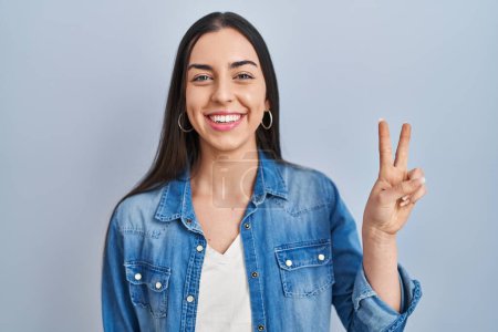 Photo for Hispanic woman standing over blue background showing and pointing up with fingers number two while smiling confident and happy. - Royalty Free Image