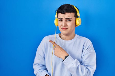Photo for Non binary person listening to music using headphones pointing aside worried and nervous with forefinger, concerned and surprised expression - Royalty Free Image