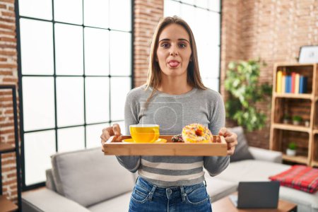 Téléchargez les photos : Jeune femme tenant plateau avec petit déjeuner nourriture langue collante heureux avec expression drôle. - en image libre de droit
