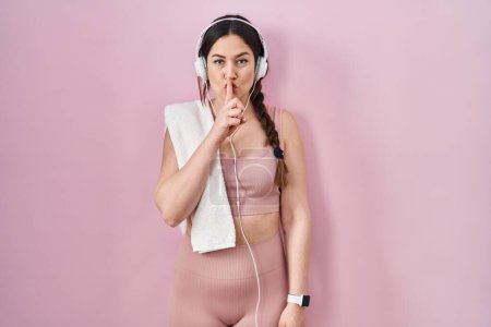 Photo for Young brunette woman wearing sportswear and headphones asking to be quiet with finger on lips. silence and secret concept. - Royalty Free Image