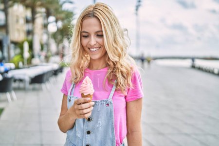 Foto de Young blonde woman smiling confident eating ice cream at seaside - Imagen libre de derechos