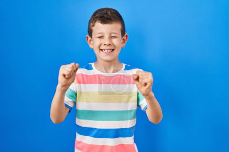 Foto de Young caucasian kid standing over blue background excited for success with arms raised and eyes closed celebrating victory smiling. winner concept. - Imagen libre de derechos