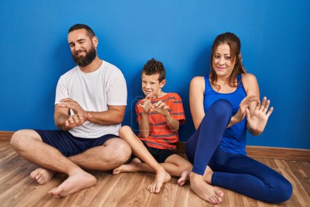 Photo for Family of three sitting on the floor at home disgusted expression, displeased and fearful doing disgust face because aversion reaction. with hands raised - Royalty Free Image