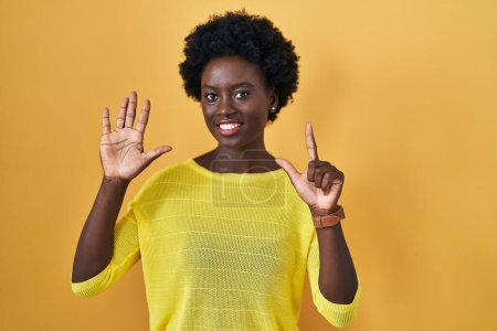 Foto de Mujer joven africana de pie sobre el estudio amarillo mostrando y señalando hacia arriba con los dedos número siete mientras sonríe confiado y feliz. - Imagen libre de derechos