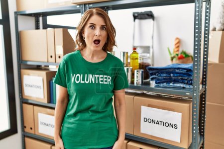 Foto de Mujer de mediana edad con camiseta voluntaria en las donaciones de pie asustado y sorprendido con la boca abierta para sorpresa, cara de incredulidad - Imagen libre de derechos