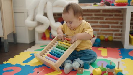 Foto de Adorable hispanic baby playing with abacus sitting on floor at kindergarten - Imagen libre de derechos