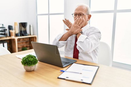 Foto de Hombre mayor que trabaja en la oficina usando la expresión de rechazo de computadora portátil cruzando brazos y palmas haciendo signo negativo, cara enojada - Imagen libre de derechos