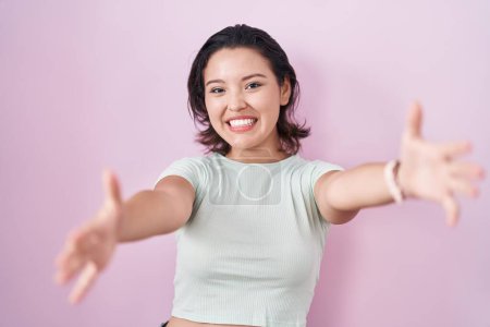 Photo for Hispanic young woman standing over pink background looking at the camera smiling with open arms for hug. cheerful expression embracing happiness. - Royalty Free Image