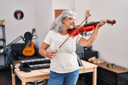 Foto de Middle age woman musician playing violin at music studio - Imagen libre de derechos