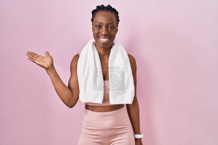 Téléchargez les photos : Beautiful black woman wearing sportswear and towel over pink background smiling cheerful presenting and pointing with palm of hand looking at the camera. - en image libre de droit